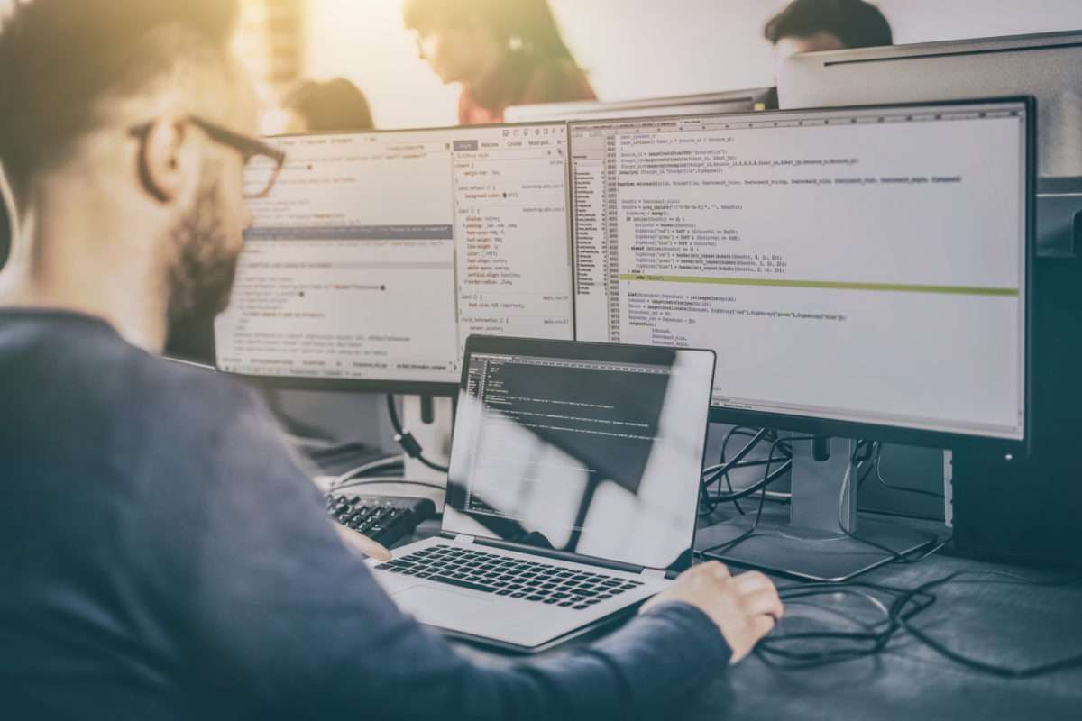 Une homme fait du code devant 3 écrans d'ordinateur